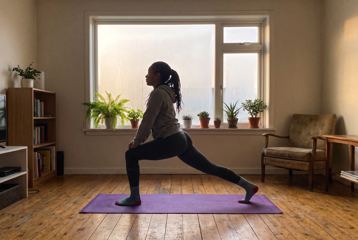 Frau dehnt sich morgens auf einer Yogamatte am Fenster